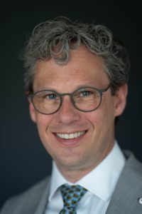 Pepijn Vemer, de voorzitter van de ECDA. Hij draagt een grijs pak met een witte blouse en gestippelde stropdas